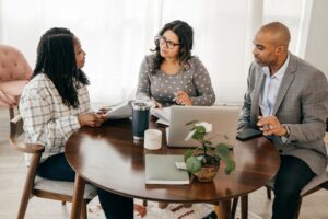 This is a photo of three people in consultation around a table. It is the header image to illustrate a news item titled 'Position statement from the Urostomy Association in response to the consultation – ‘Medical Devices in Primary Care Proposals for Updating Part IX of the Drug Tariff’.