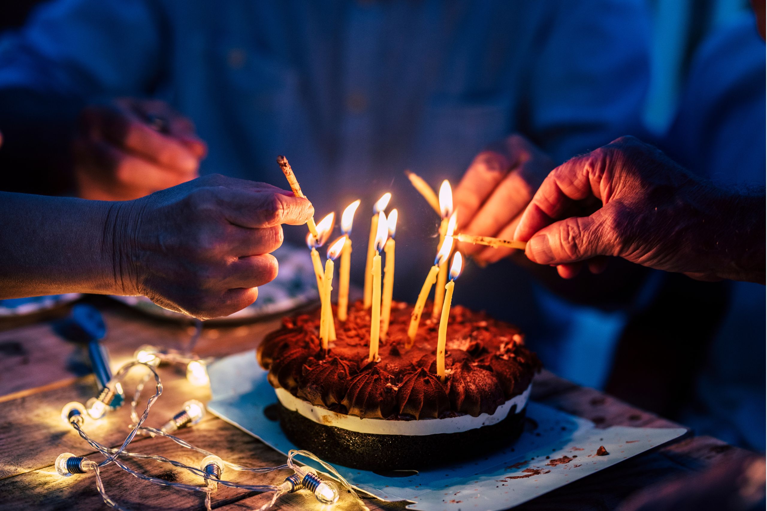 This is a photo of a birthday cake, with candles being lit. It is the header image of a page on the Urostomy Association's website which encourages readers to donate in celebration.
