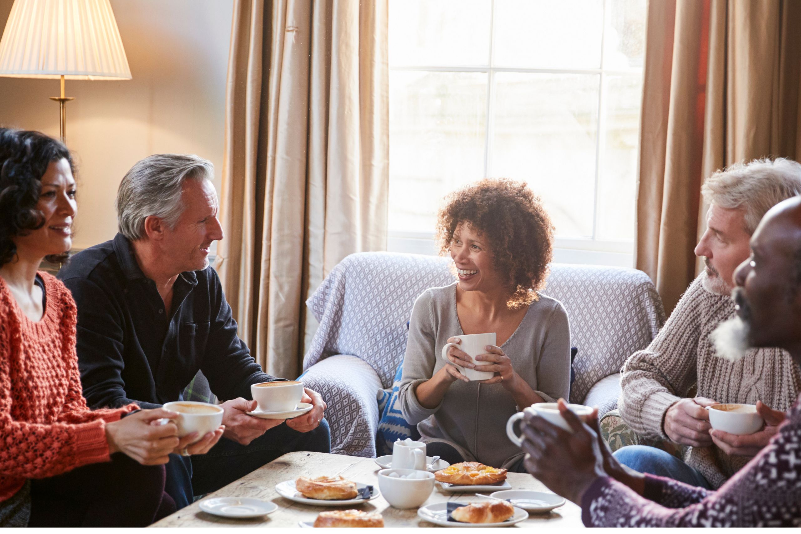 This is a photo of a group of five people chatting around a coffee table. It is the header image for the 'About us' page on the Urostomy Association's website.