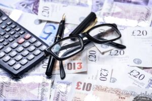 This is a photo of some sterling currency, plus fountain pen, calculator and reading glasses. It is the header image for the 'Could you be our next treasurer' page on the Urostomy Association's website.