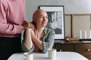 This is a photo of a woman in a head scarf being comforted by another woman standing by. It is the header image for an article on the Urostomy Association's website entitled: 'Joining Cancer52 in launching a manifesto for rare and less common cancers'