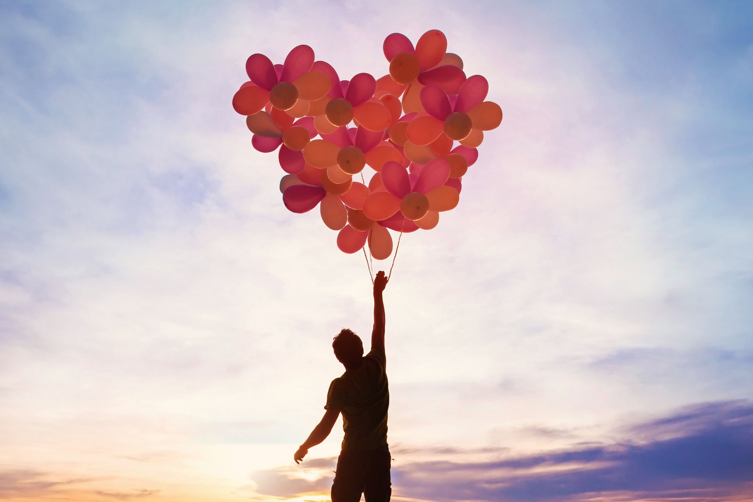 This is a photo of a person at sunset holding a bunch of balloons which make up a heart shape. It is the header image for the Urostomy Association's Help provide hope appeal page