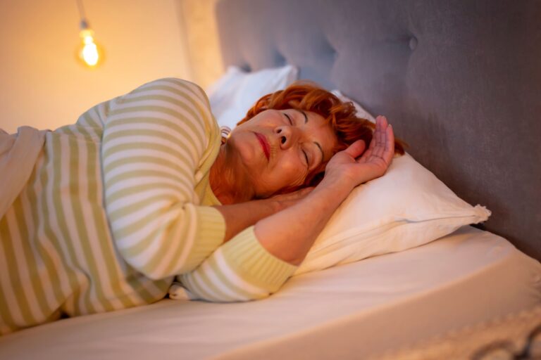 This is a photo of a woman wearing a white and yellow striped top. She is asleep in bed. It is the header image for the page on the Urostomy Association's website linking through to its webinar on managing night drainage