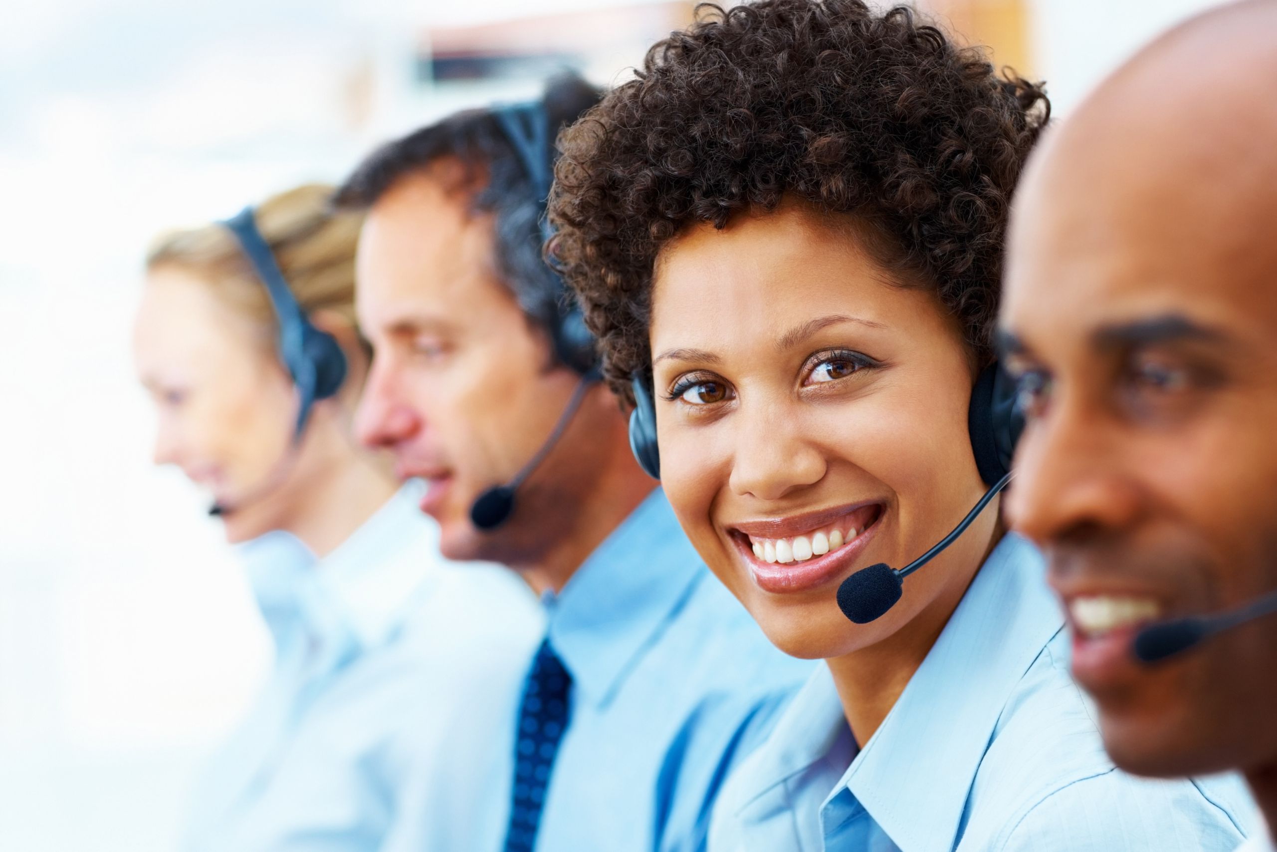 This photo shows four people answering telephone calls. They're each wearing mouth pieces. There is a young woman facing the camera. It is the header image for a page on the Urostomy Association's website entitled 'stoma product delivery: know your rights'