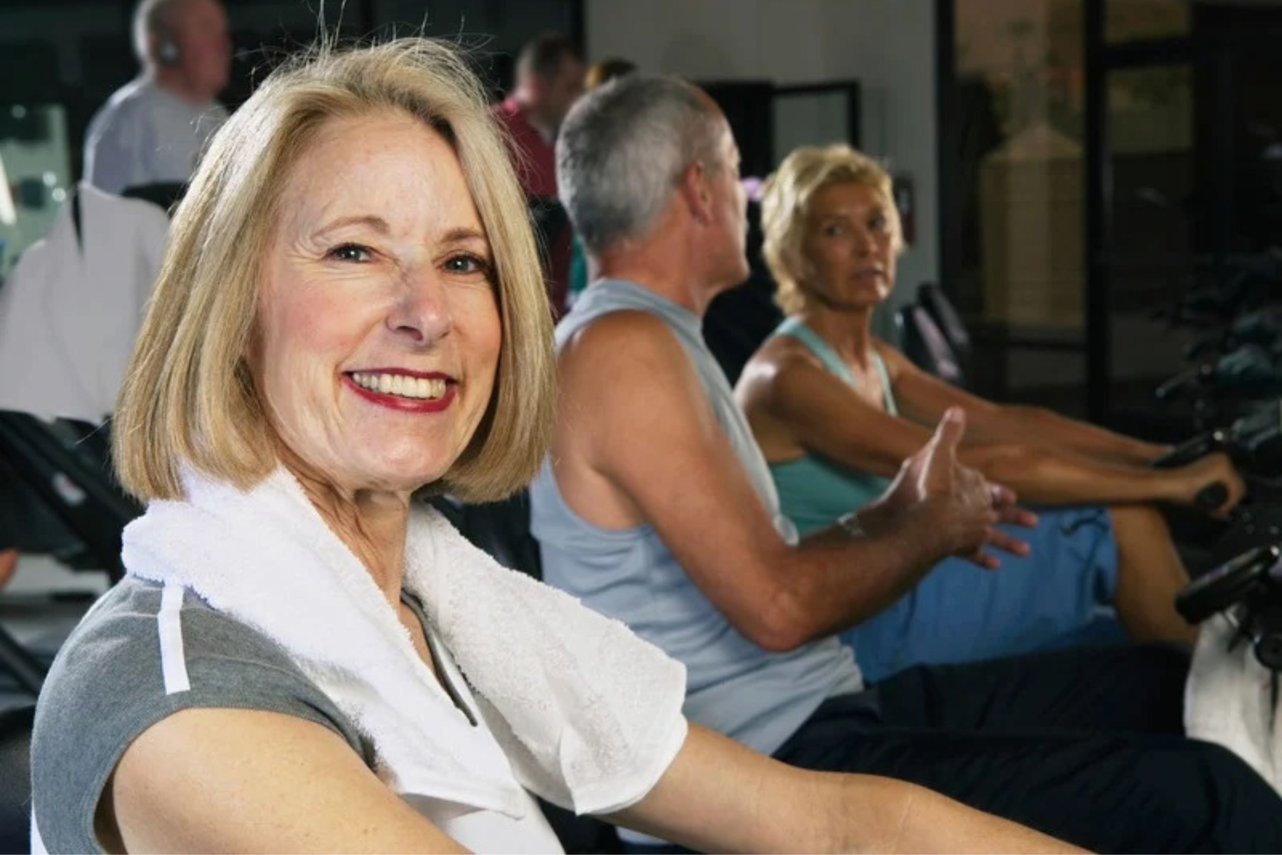 This is a photo of three people in an exercise class. The woman in the foreground is smiling at the camera and has a towel around her neck. It is the header image for a page called 'Help for hernias' on the Urostomy Association's website