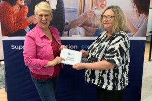 This is a photo of Samantha Sherratt, the Urostomy Association's Transformation Director, with Pauline Jones, the Company Secretary for The Hospital Saturday Fund. Pauline is presenting Samantha with an envelope confirming a grant toward the Association's Help Provide Hope fund,.