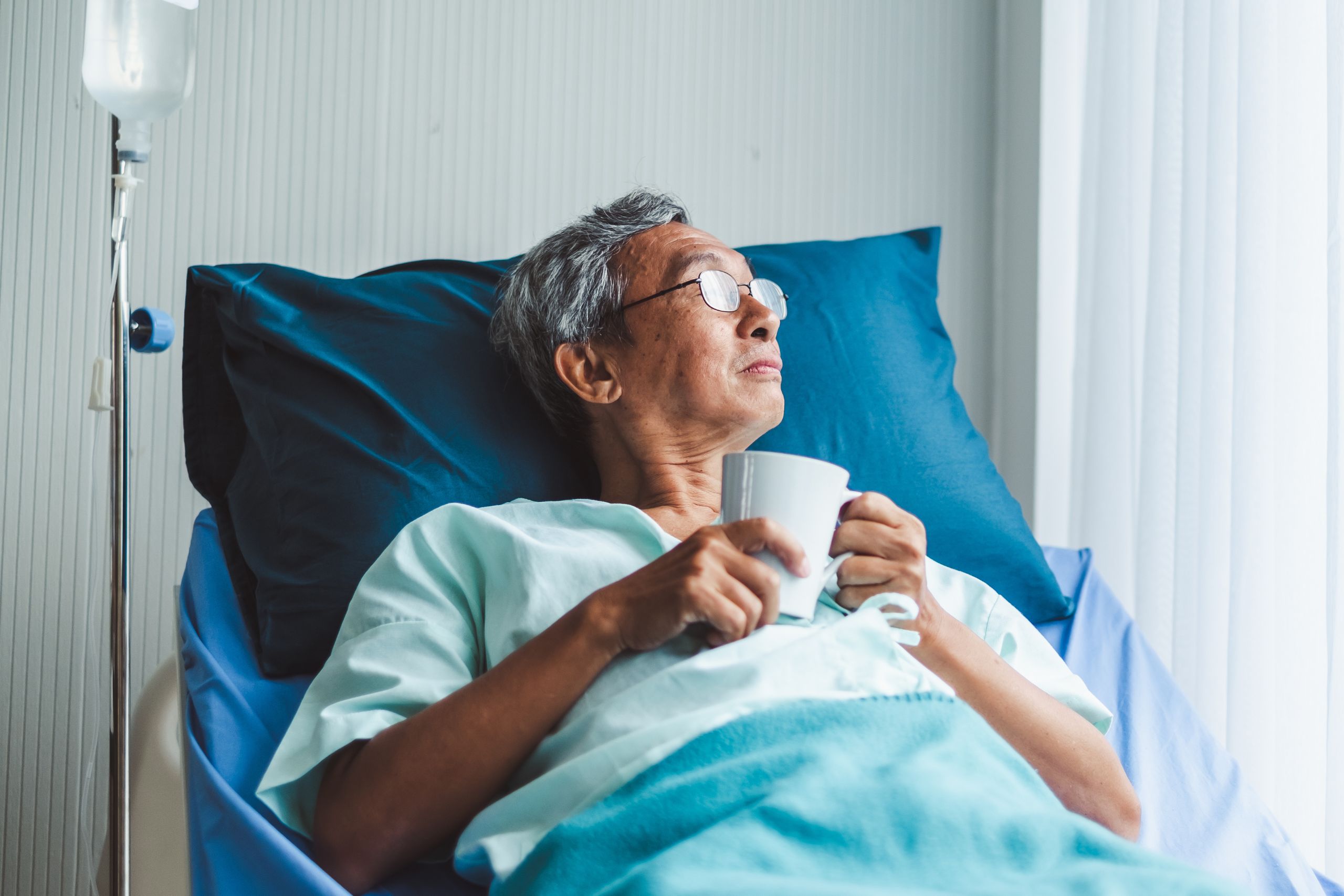 This is a photo of someone propped up in a hospital bed so they can drink a cup of tea and look out of the window.