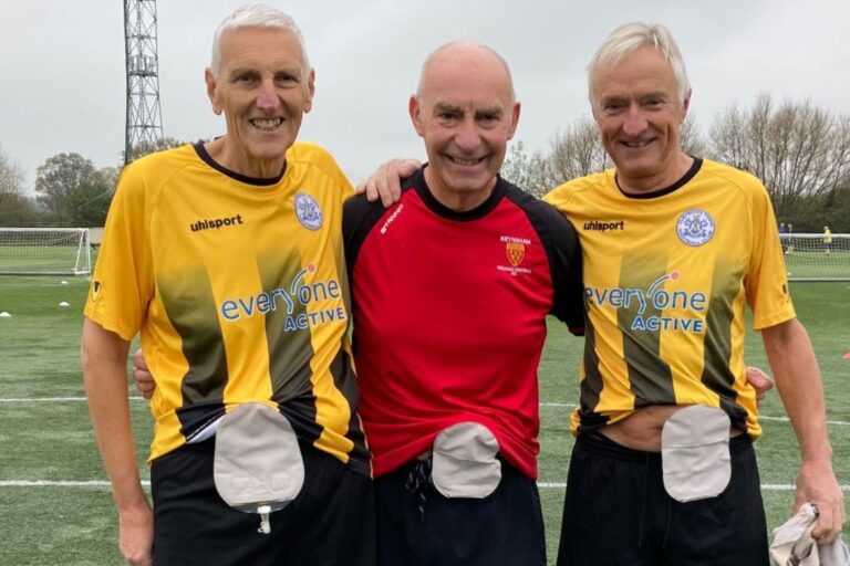 This is a photo of urostomate Jonathan Fry on the left. He is standing next to fellow ostomates Gary and Derek. They are each in football kit, and have their ostomy bags showing.