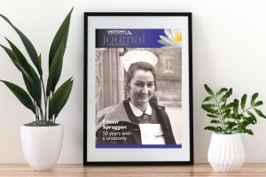 This photo is of a picture frame sitting on a wooden table. In the frame is the cover of Summer14's edition of the Urostomy Association Journal, featuring Eileen Spraggon.