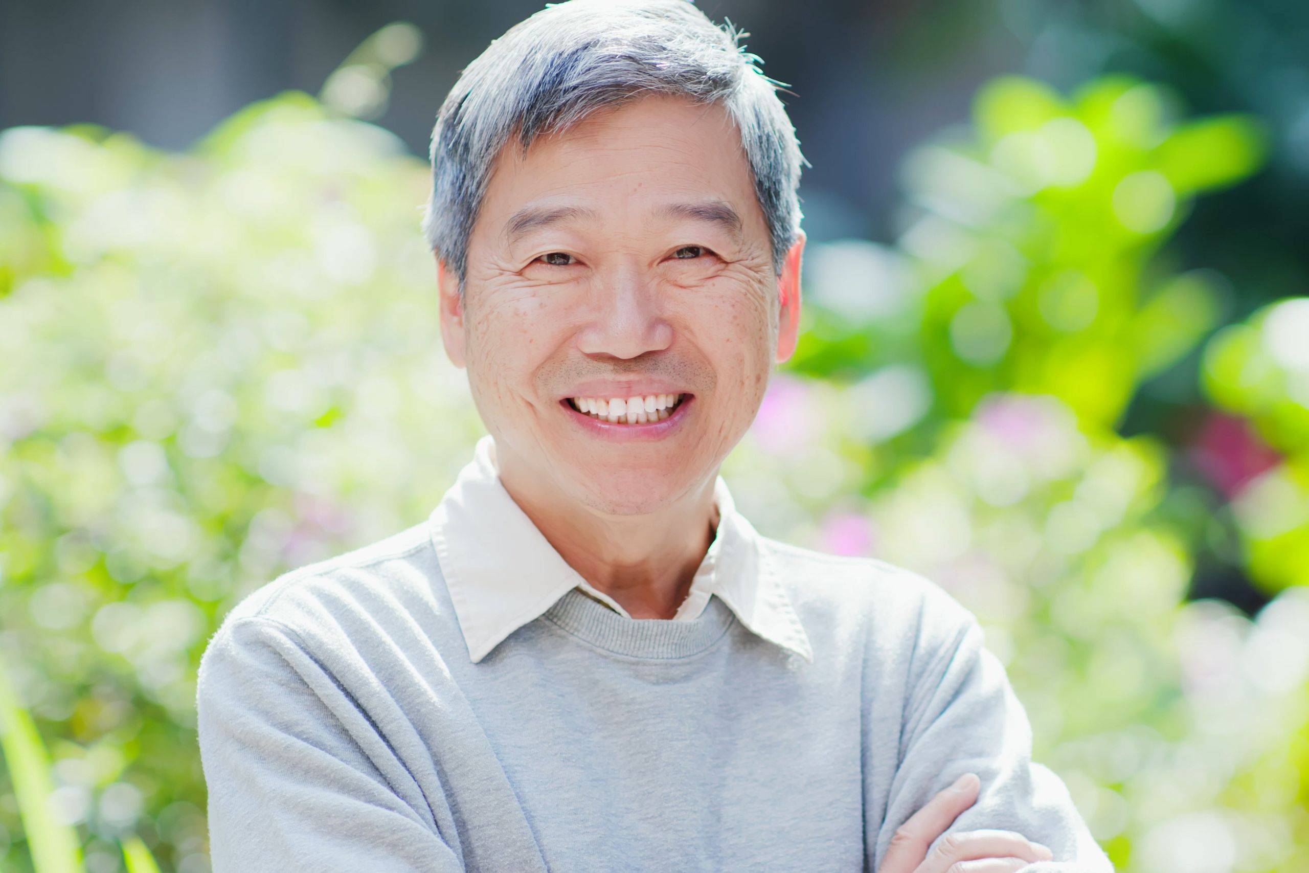 This is a photo of a middle aged man smiling directly at the camera. He is in a garden with lush green plants behind him. It is the primary image for the information page on the Urostomy Association's website relating to continent urinary diversions / internal pouches / Mitrofanoffs