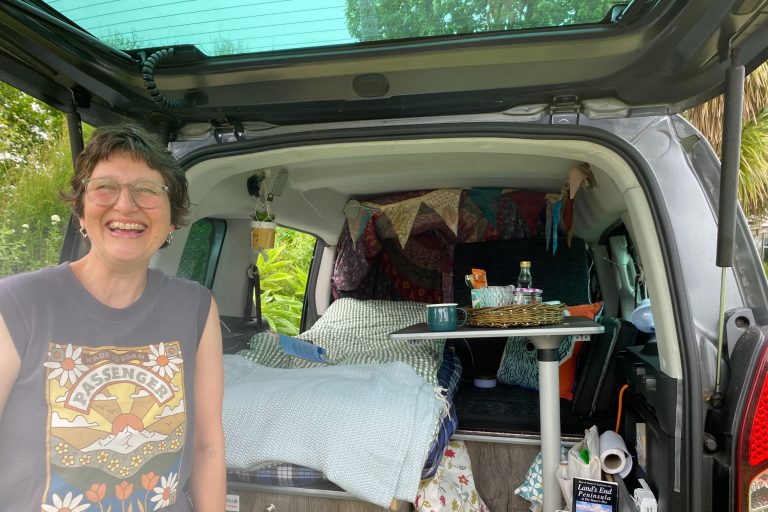This is a photo of Ruth Taylor standing in front of her 'micro camper'. The boot is open and she is smiling at the camera