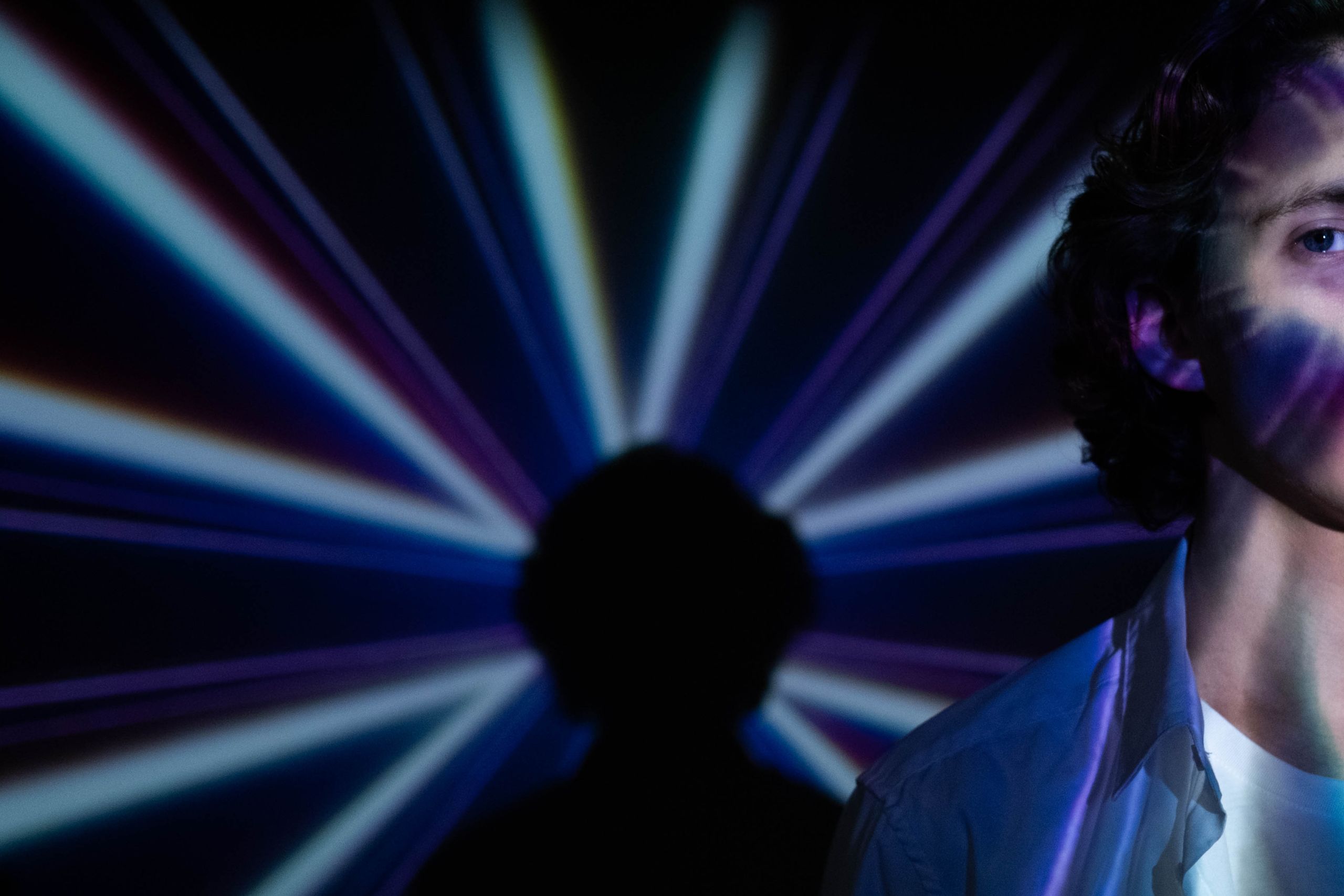 This photo depicts a nightclub scene. There are strobe lights in the background. In the foreground, to the right of the picture, is a young man facing the camera.