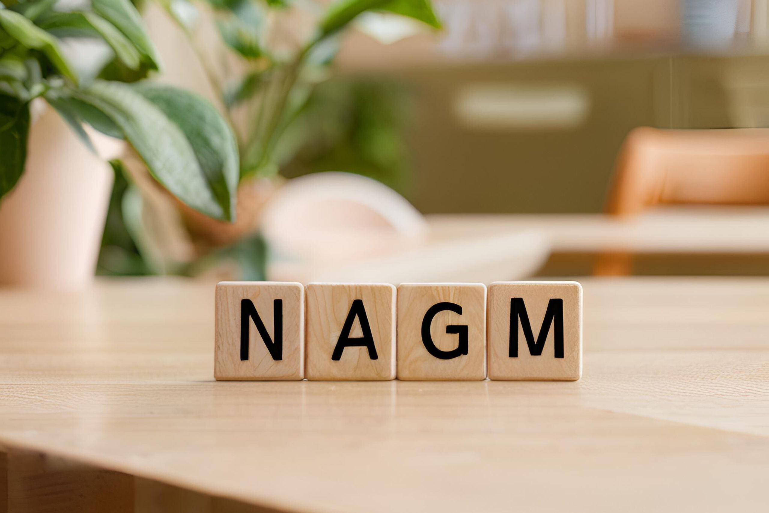 This is a photo of four scrabble tiles on a wooden table. The letters are NAGM.