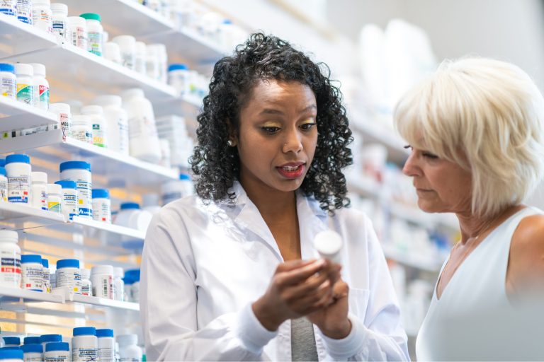 This is a photo set in a pharmacy. A young pharmacist is explaining the labelling on a pill bottle to a customer