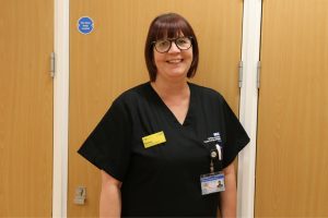 This is a photo of Donna Wilson. She's wearing a black nurses uniform top, and she's standing in front of some vinyl wooden doors in a hospital.