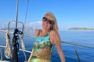 This is a photo of Urostomate, Jackie Hannay, sitting on a boat in her swimming costume. She's wearing sunglasses and facing the camra. There's blue sea and sky behind her.