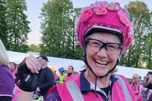 This photo is of the blog's author, Maureen. She is wearing a pink outfit for cycling, and has a crocheted cover on her helmet.