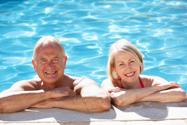 This photo is of a couple in the pool. They are at the edge, smiling to the camera.