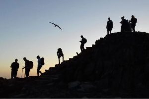 This photo shows eight people on a hill at sunrise. They are silhouetted..